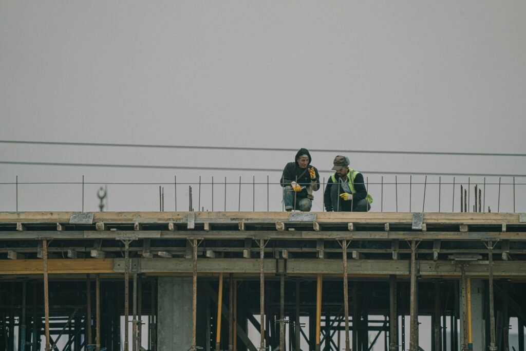 Two construction workers on a building site in Denizli, Türkiye, working under overcast skies.